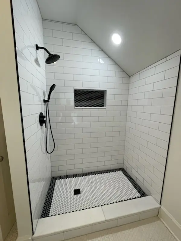 Finished attic shower with marble curb and penny-tile border