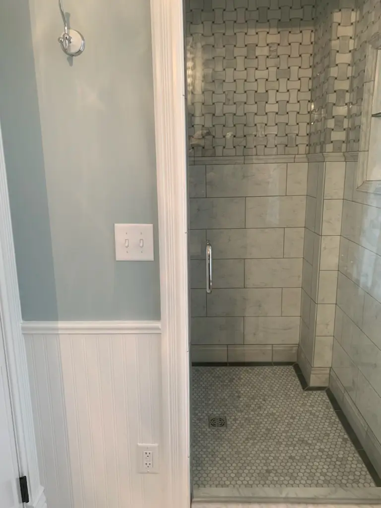 Shower with basketweave accent tile seen from the hall, beadboard wainscot