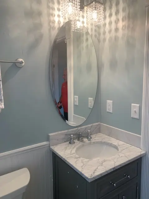 Oval mirror over a marble-top vanity with beadboard wainscot