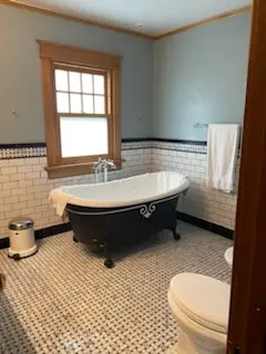 Black clawfoot tub with subway-tile wainscot and basketweave floor