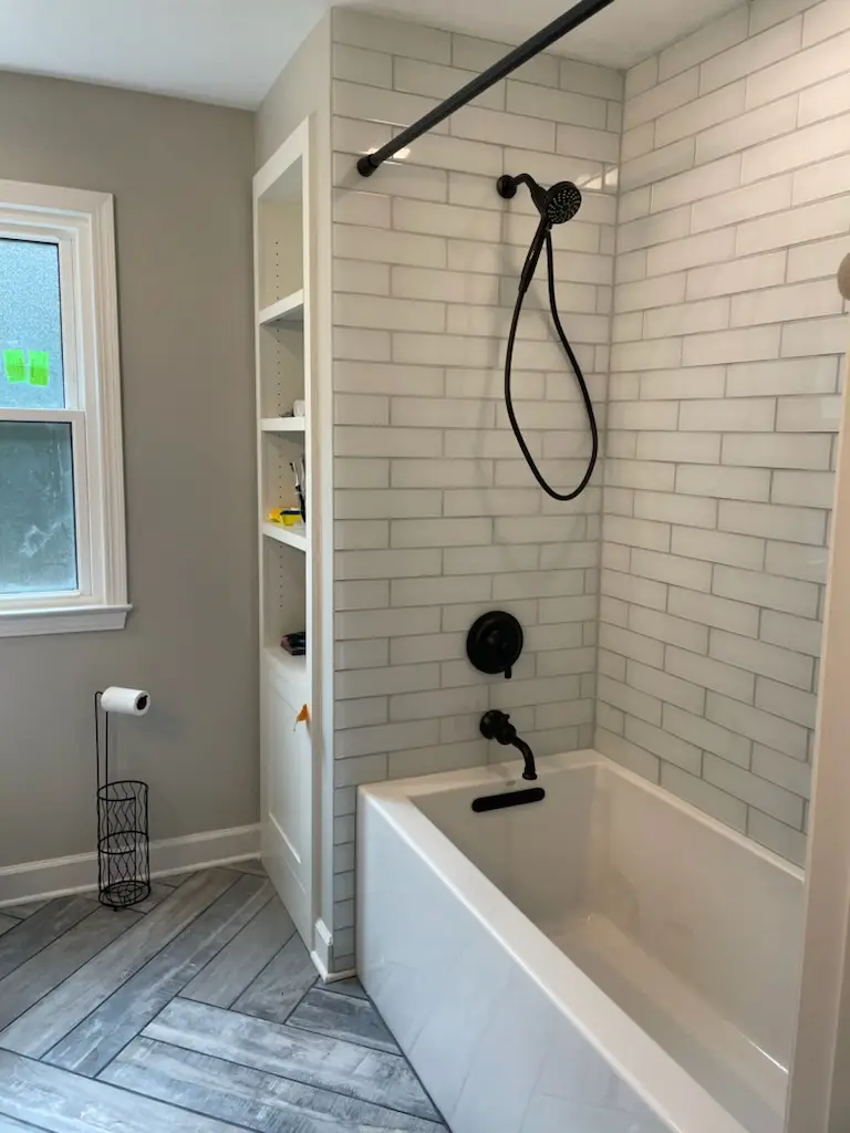 Tub with white subway tile, black fixtures, and herringbone floor