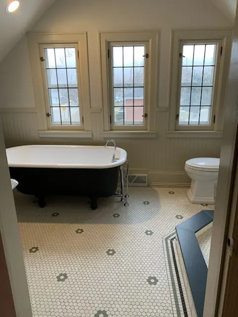 Clawfoot tub under three leaded-glass windows with hex flower floor