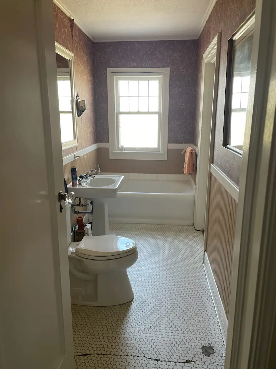 Before: built-in tub under a tall window, wallpaper and hex floor